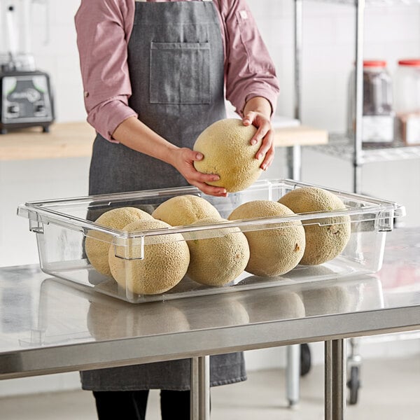 A woman in an apron holding a Cambro clear food storage container of melons.