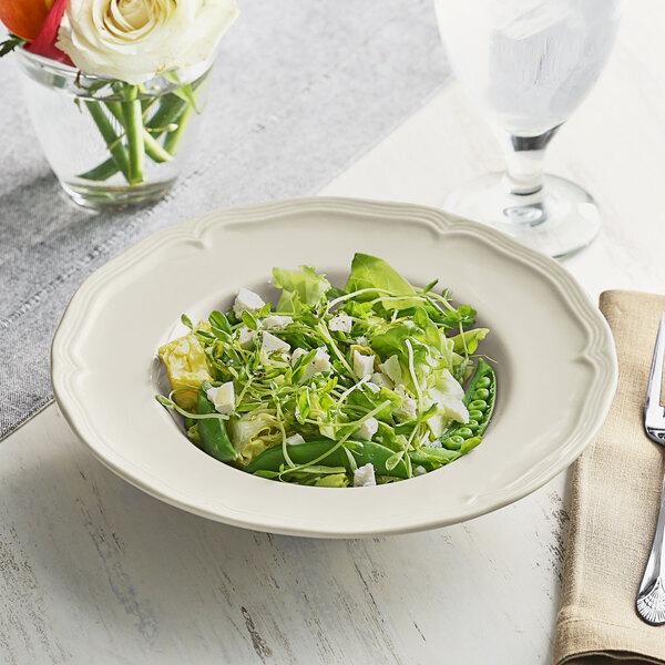 An Acopa Condesa warm gray porcelain bowl filled with green salad on a white table.