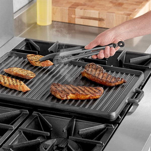 A person using Valor cast iron griddle to cook steak on a grill.