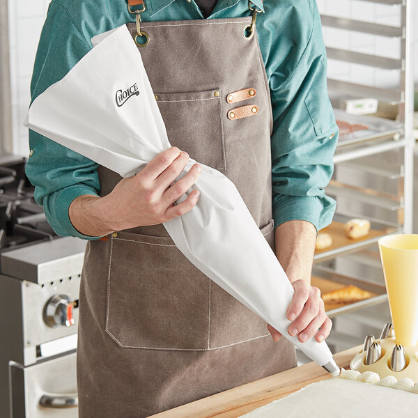 A person in an apron holding a Choice plastic coated canvas pastry bag.