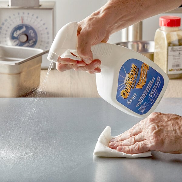 A person spraying Noble Chemical QuikSan surface sanitizer on a counter.