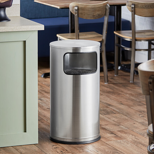 A Lancaster Table & Seating stainless steel round decorative trash can on a wood floor.