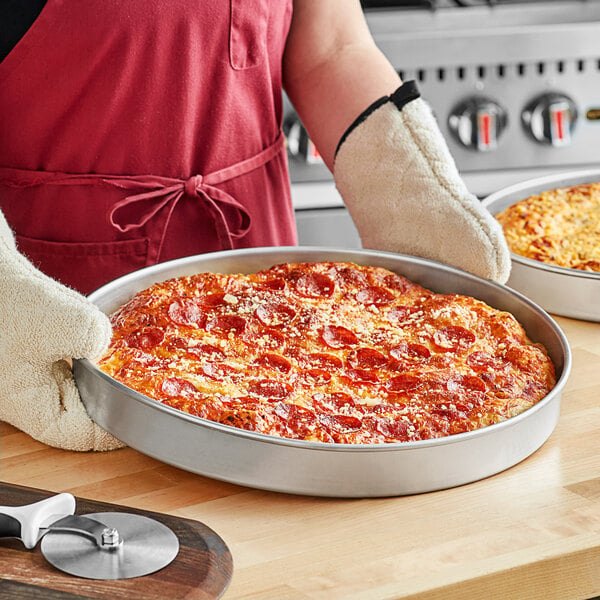 A person holding a pepperoni pizza in a Choice aluminum deep dish pizza pan.