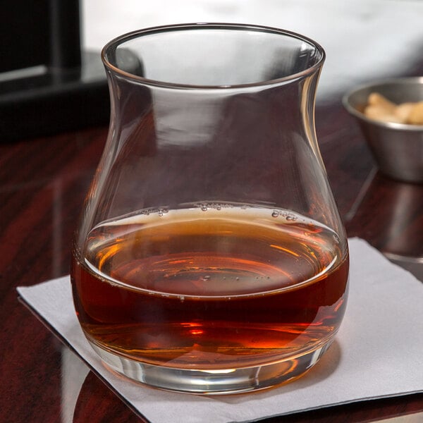A Stolzle Canadian Whiskey Glass filled with brown liquid sits on a table next to a glass of water.
