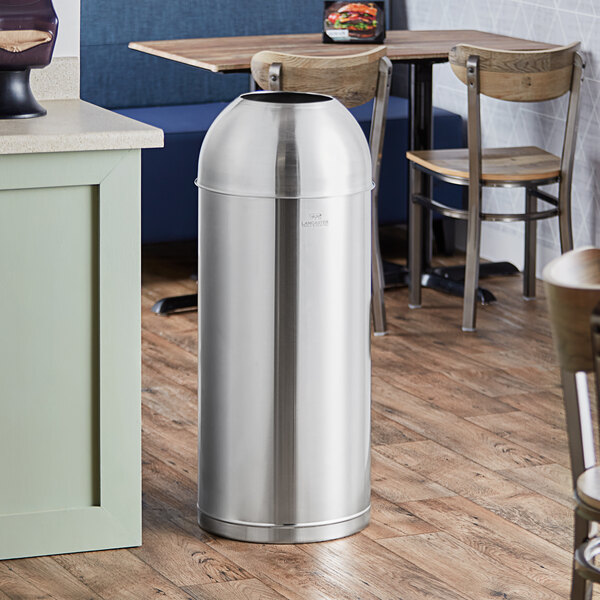 A Lancaster Table & Seating stainless steel decorative waste receptacle with an open dome lid on a wood floor.
