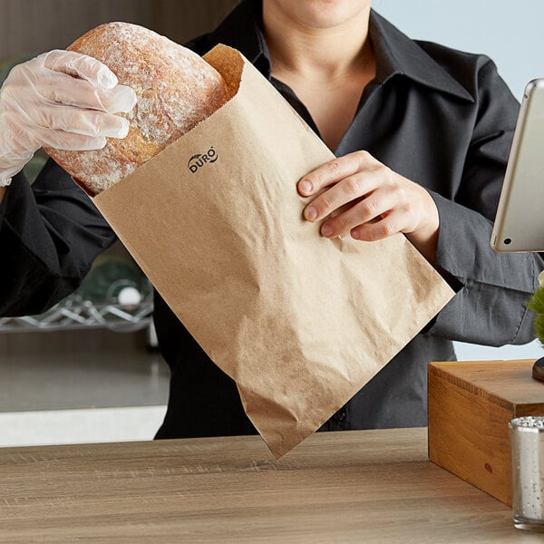 A person holding a Duro brown merchandise bag with a loaf of bread.
