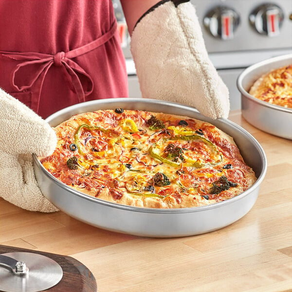 A person holding a pizza in a Choice aluminum deep dish pizza pan.