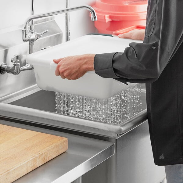 A hand using a white Choice polypropylene bus tub to wash dishes in a sink.
