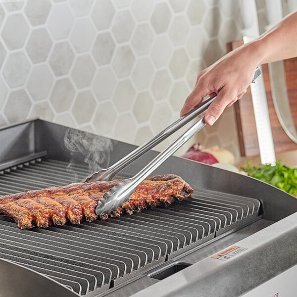 A pair of Choice stainless steel tongs holding ribs on a grill.