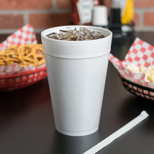 A white Dart foam cup with a lid and a straw in a cup of soda with ice.
