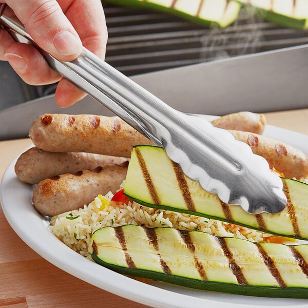 A person using Choice stainless steel utility tongs to serve zucchini on a plate of food.