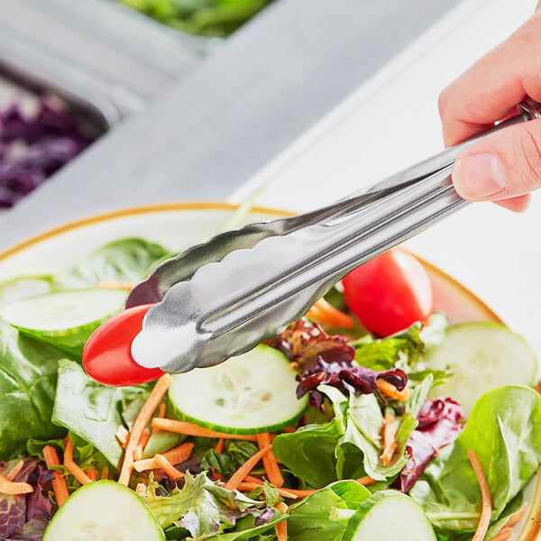 A person using Choice heavy-duty stainless steel utility tongs to serve salad
