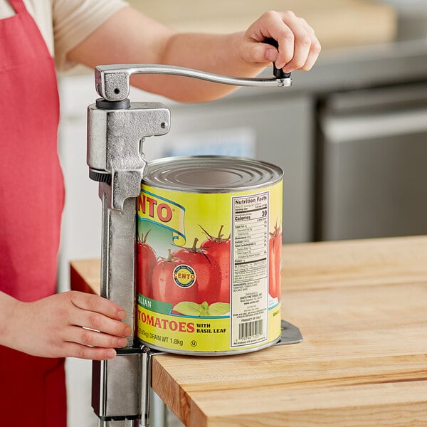 A person using a Choice Prep Standard Duty manual can opener with a stainless steel base to open a can on a counter.