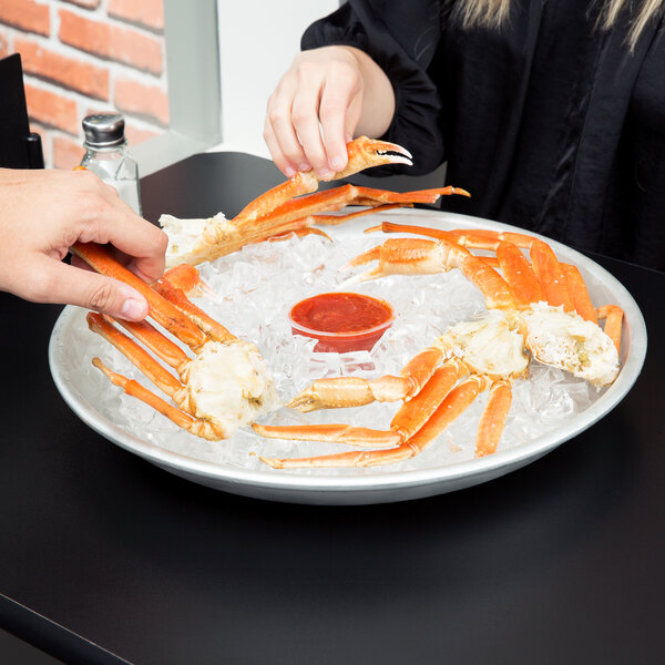 A person holding an American Metalcraft aluminum seafood tray with crab legs.