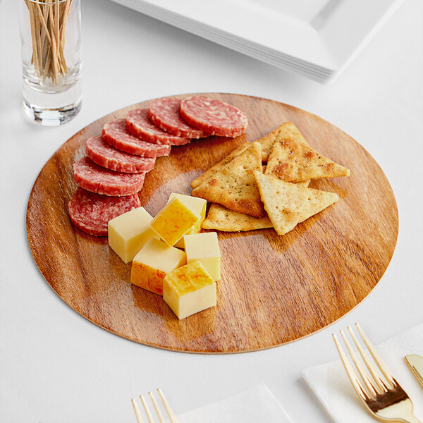 A wooden Enjay charcuterie board with cheese, crackers, and a fork on a table.