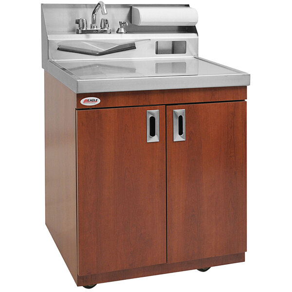 A brown laminate cabinet with a stainless steel top and wheels with a sink and faucet inside.