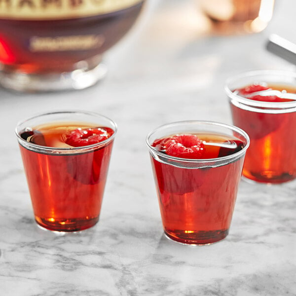 A group of Choice clear plastic shot glasses filled with red liquid and berries on a table.