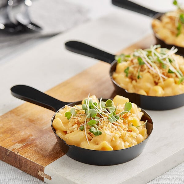 A row of Choice black plastic mini frying pans filled with macaroni and cheese.