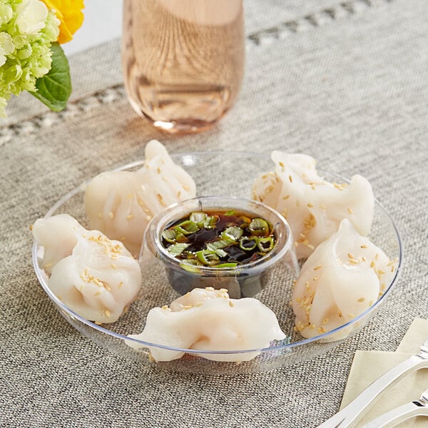 A clear plastic mini circular dip tray with dumplings and sauce.