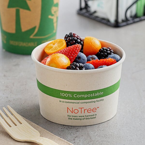 A World Centric compostable paper cup filled with fruit next to a wooden fork.