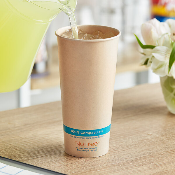 A pitcher pouring liquid into a World Centric compostable paper cup on a table.