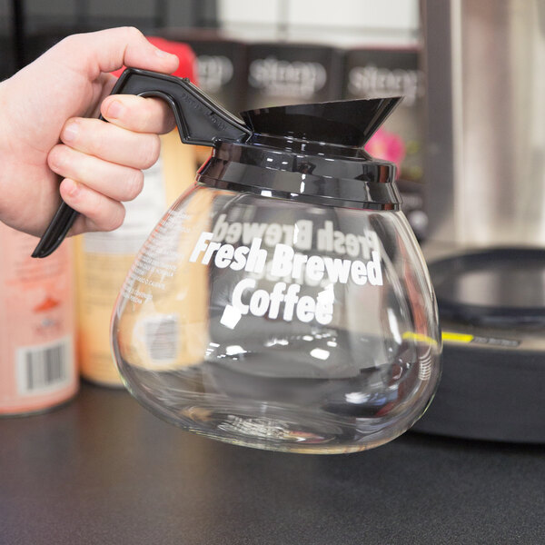 A hand holding a Grindmaster glass coffee decanter with a black handle.