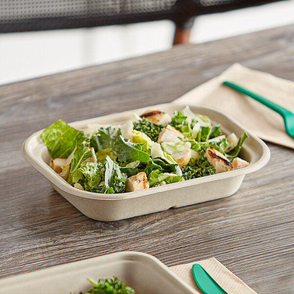 A World Centric compostable fiber container filled with a salad on a table with a green fork.