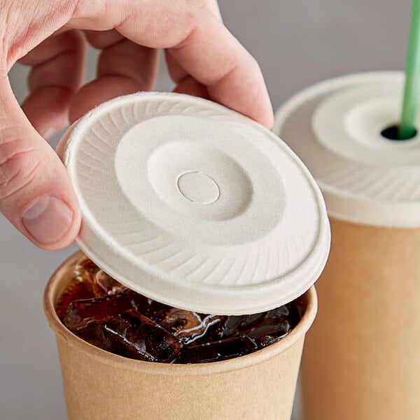 A hand holding a World Centric fiber cold cup lid over a cup of ice.