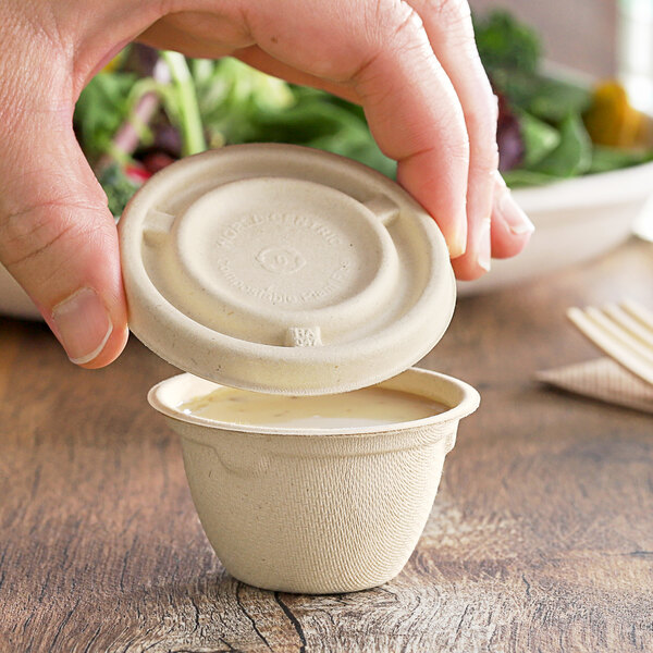 A person holding a small World Centric compostable fiber container with a white lid.