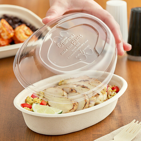 A hand placing a World Centric clear compostable plastic lid over a bowl of food.