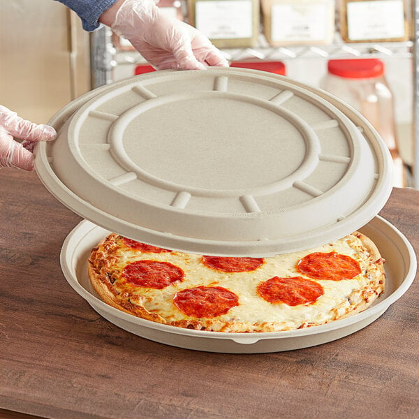 A person holding a pizza in a container with a white World Centric compostable fiber lid.