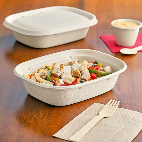 A white World Centric compostable fiber container with food and a wooden fork on a napkin.