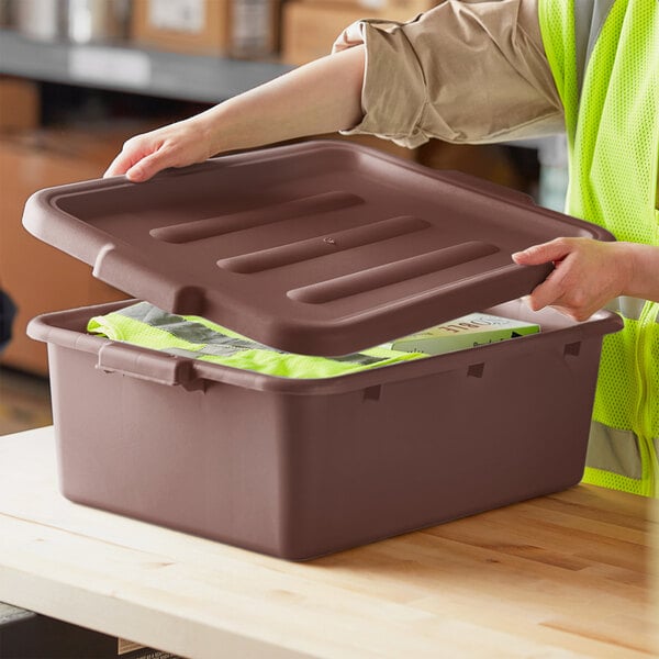 A woman in a safety vest opens a brown Lavex plastic lid.