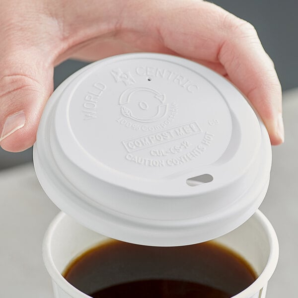 A hand using a World Centric white plastic lid to cover a white plastic cup of coffee.