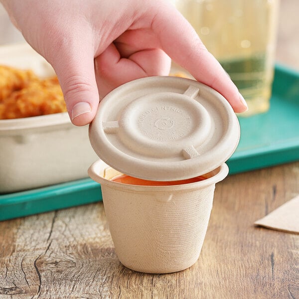 A hand holding a World Centric compostable fiber lid over a small white container.