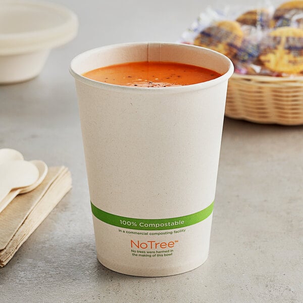 A World Centric compostable paper food cup filled with soup on a table next to a basket of cookies.