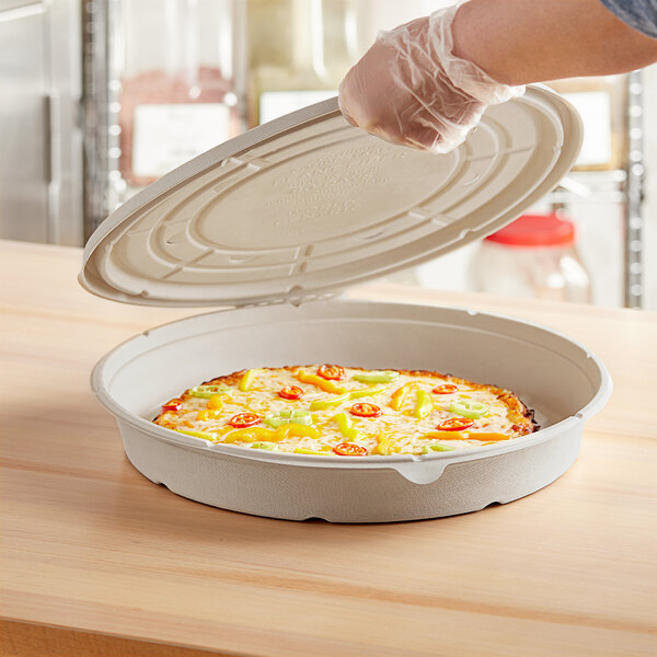 A person putting a pizza into a World Centric compostable fiber pizza container.