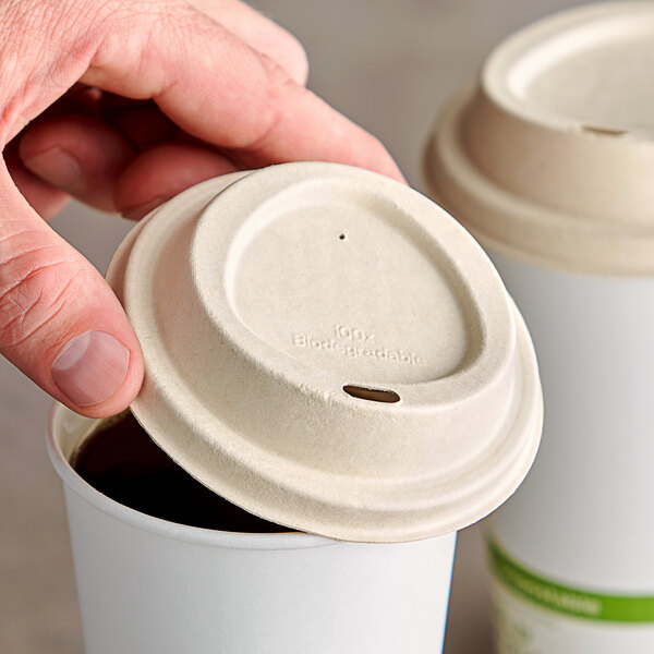 A hand holding a World Centric fiber hot cup sip lid over a coffee cup.