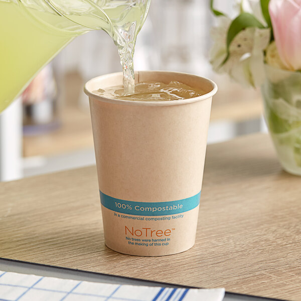 A glass pitcher pouring liquid into a World Centric compostable paper cup on a table.