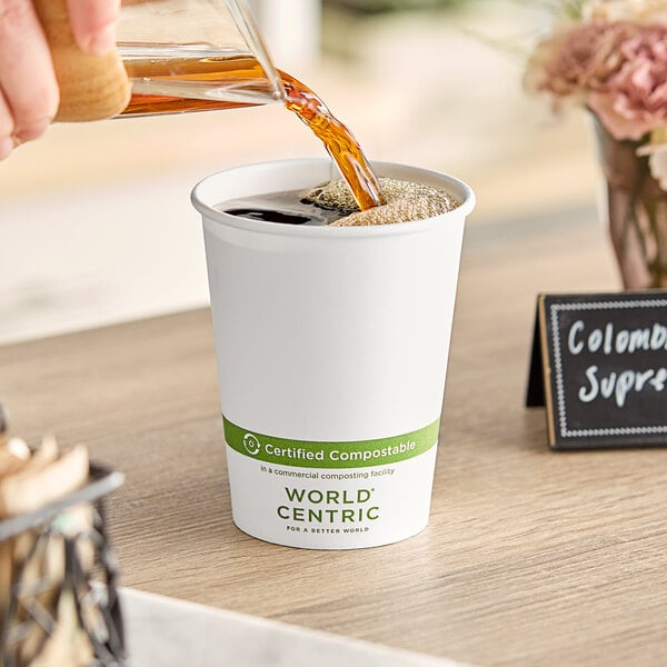 A person pouring compostable coffee into a World Centric white paper hot cup.