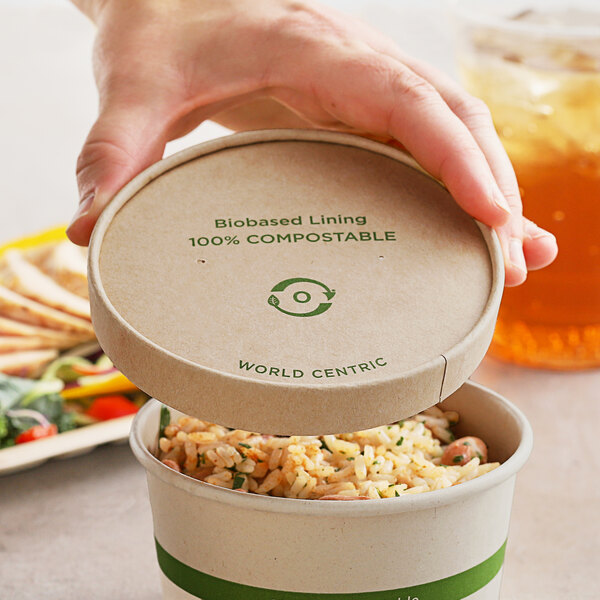 A hand holding a World Centric compostable paper container with a Kraft lid.