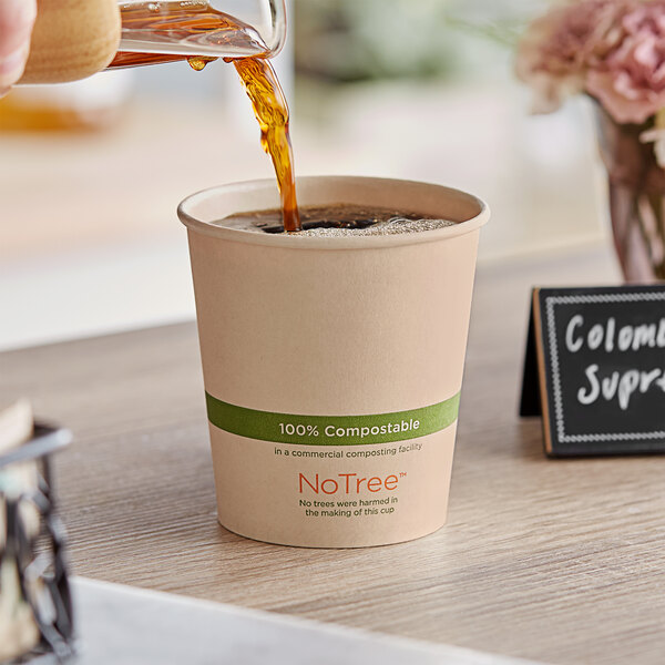 A person pouring coffee into a World Centric natural compostable paper hot cup on a table in a coffee shop.