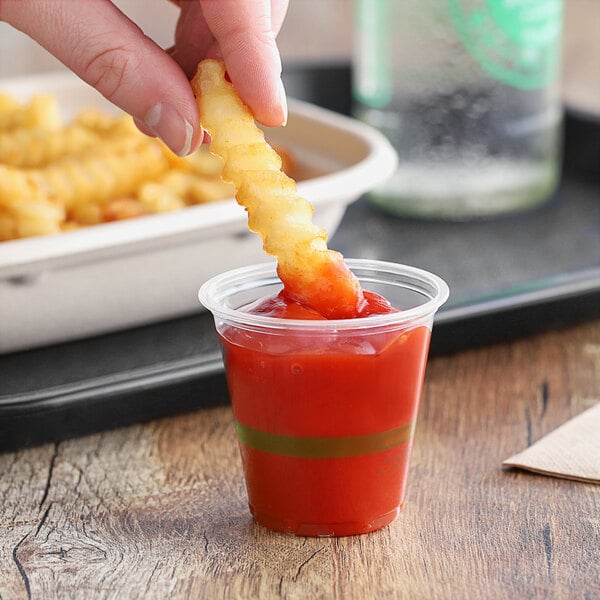 A hand holding a World Centric compostable plastic cup with ketchup and a french fry in it.