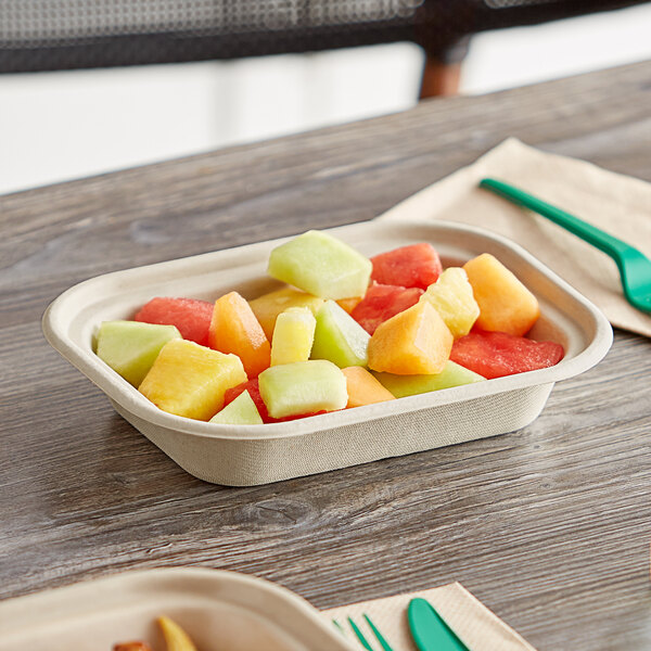 A World Centric compostable fiber container filled with fruit on a table with a spoon and fork.