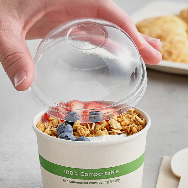 A hand placing a World Centric clear plastic lid on a bowl of food.