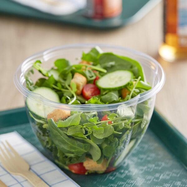 A salad in a World Centric clear plastic deli bowl with a wooden fork on a napkin.