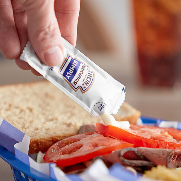 A person holding a Heinz Simply Mayonnaise packet over a sandwich.