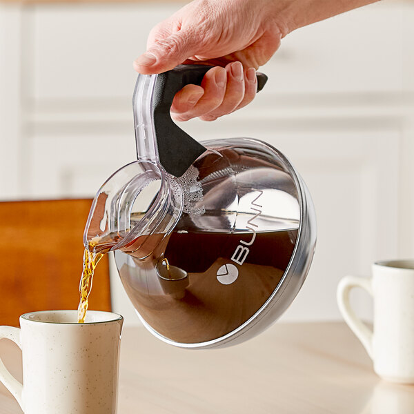 A person pouring coffee from a Bunn Easy Pour Coffee Decanter with a black handle into a white mug.