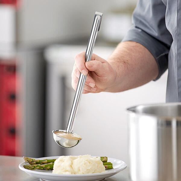 A person using a Choice stainless steel ladle to serve food onto a plate.