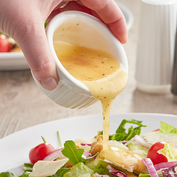 A person pouring Kraft Golden Italian dressing on a salad at a table in a salad bar.